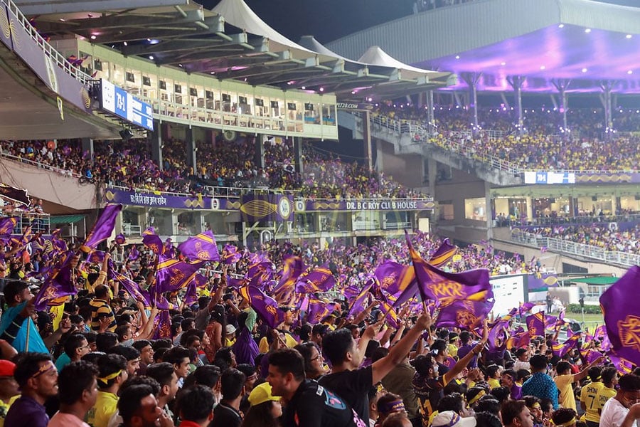 Packed cricket stadium with Kolkata Knight Riders (KKR) fans waving purple flags during an IPL match, creating a vibrant and energetic atmosphere under stadium lights.