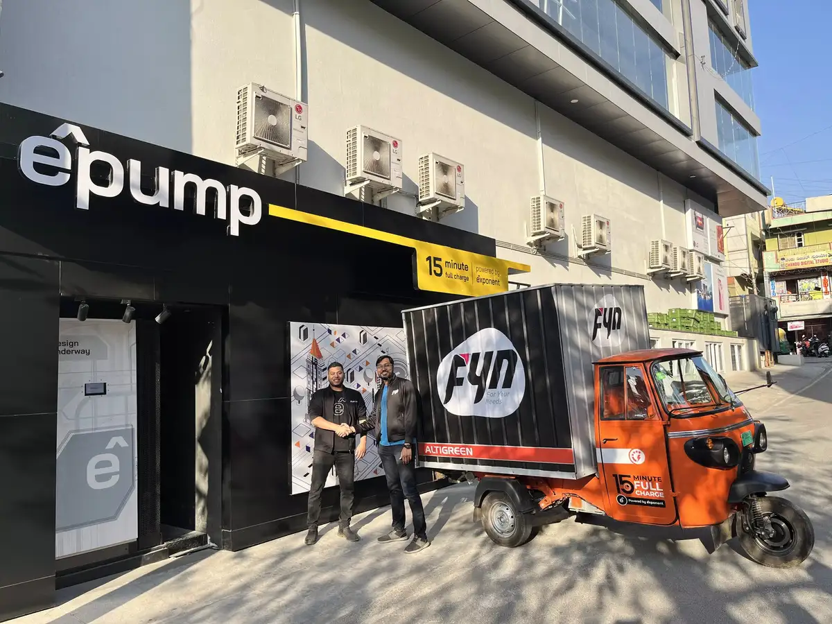Electric vehicle charging station êpump with Fyn electric cargo rickshaw and staff outside, promoting 15-minute full charge capability in an urban Indian setting.