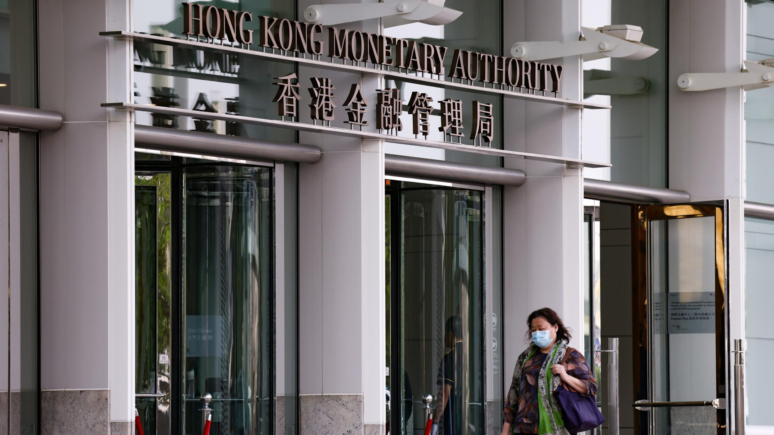 Hong Kong Monetary Authority entrance with signage in English and Chinese and a woman wearing a face mask exiting the building