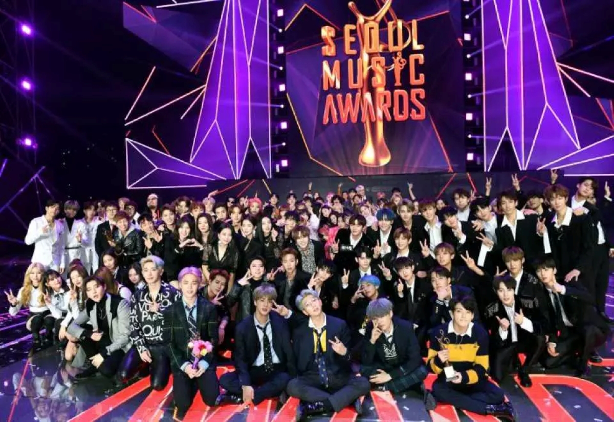 Group photo of K-pop artists and idols posing on stage at the Seoul Music Awards, with a large illuminated backdrop reading 'Seoul Music Awards' in bold letters.