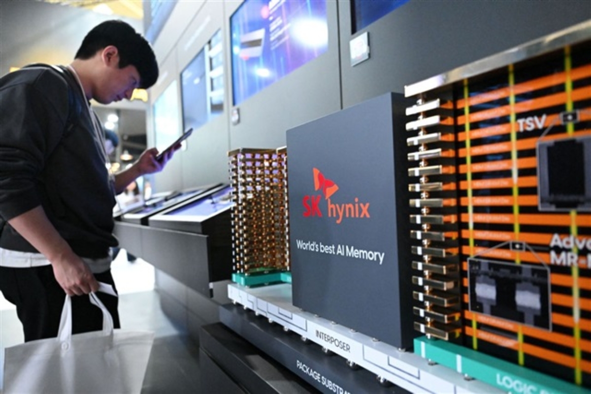 A visitor at a tech exhibition looks at a display showcasing SK hynix's AI memory technology. The large signage on the exhibit reads “SK hynix - World's best AI Memory,” with stacked memory chip modules and advanced semiconductor components shown in the foreground. The setting appears modern and high-tech, with digital panels and blue lighting.