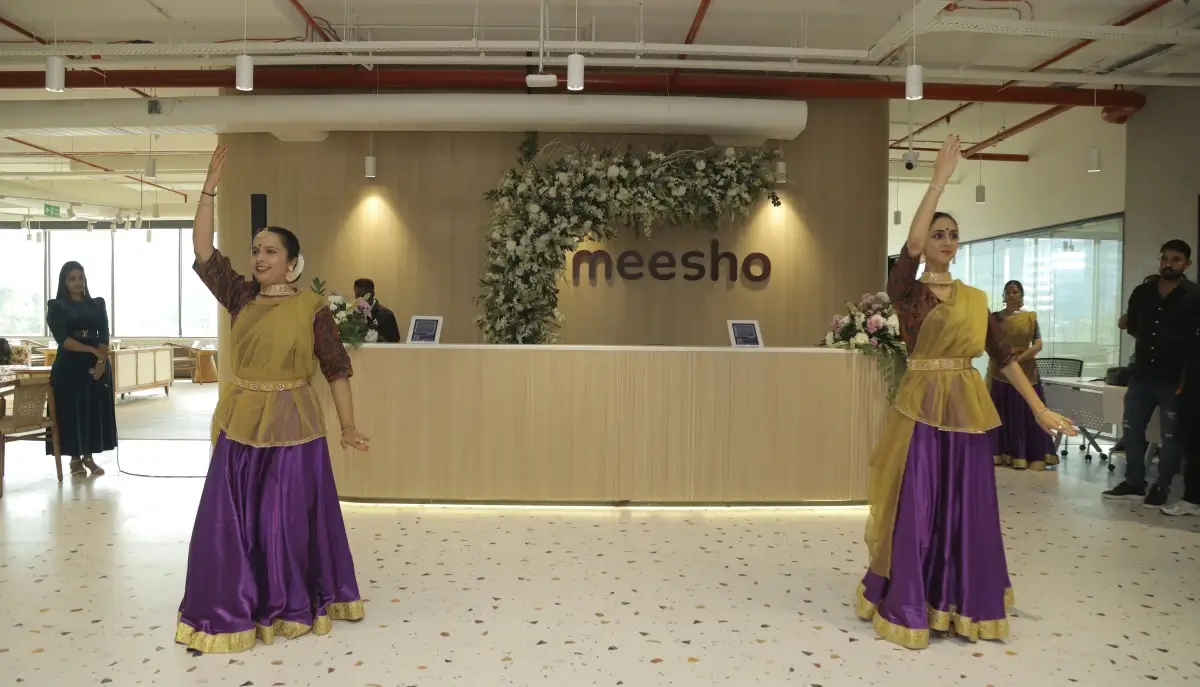 Traditional Indian dancers performing in ethnic attire during a cultural celebration at Meesho’s office reception area, decorated with flowers and branding.