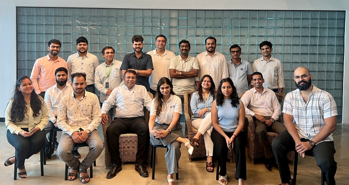Group photo of a professional business team posing indoors against a modern glass-block wall, representing a diverse corporate workforce in formal and semi-formal attire.