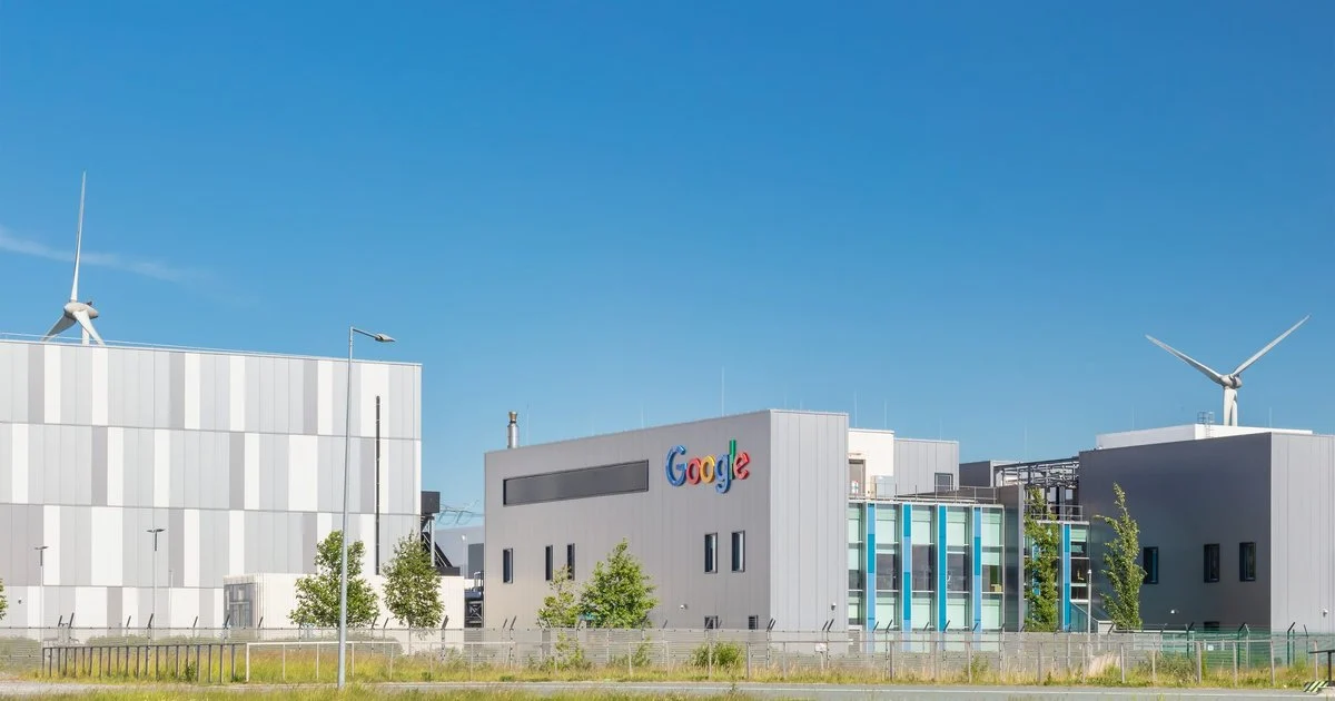 Google data centre facility with modern grey architecture and on-site wind turbines, showcasing the company’s commitment to renewable energy and sustainable cloud infrastructure.