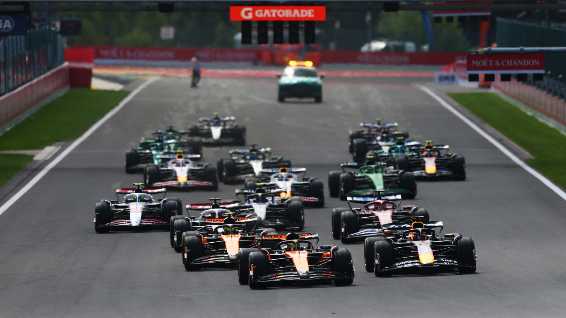 Formula 1 cars racing at the start of a Grand Prix, with McLaren and Red Bull leading the pack on the track.