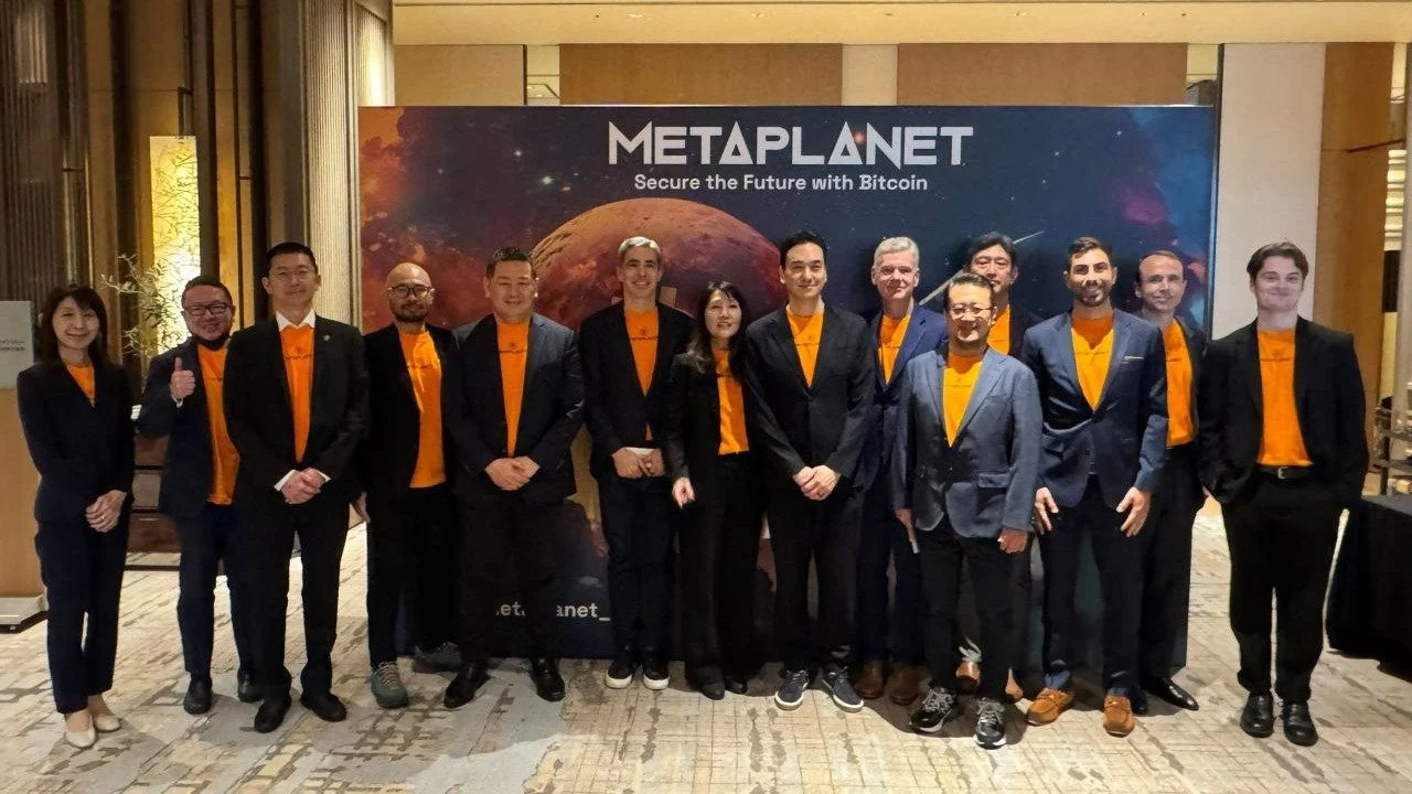 Metaplanet team posing at a corporate event with a Bitcoin-themed backdrop, highlighting the company’s focus on digital assets, blockchain investment, and securing the future with cryptocurrency.
