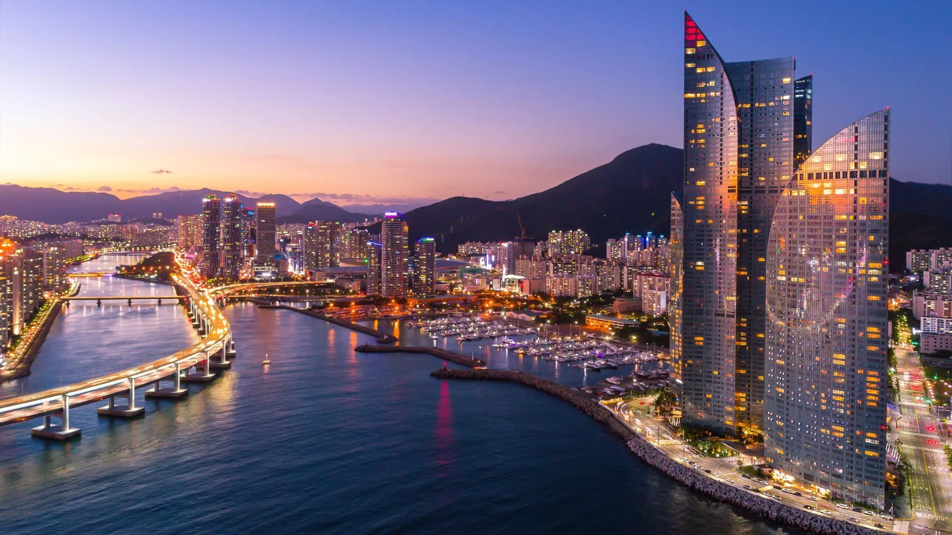 Busan city skyline at dusk with skyscrapers, Gwangan Bridge, and illuminated waterfront in South Korea.