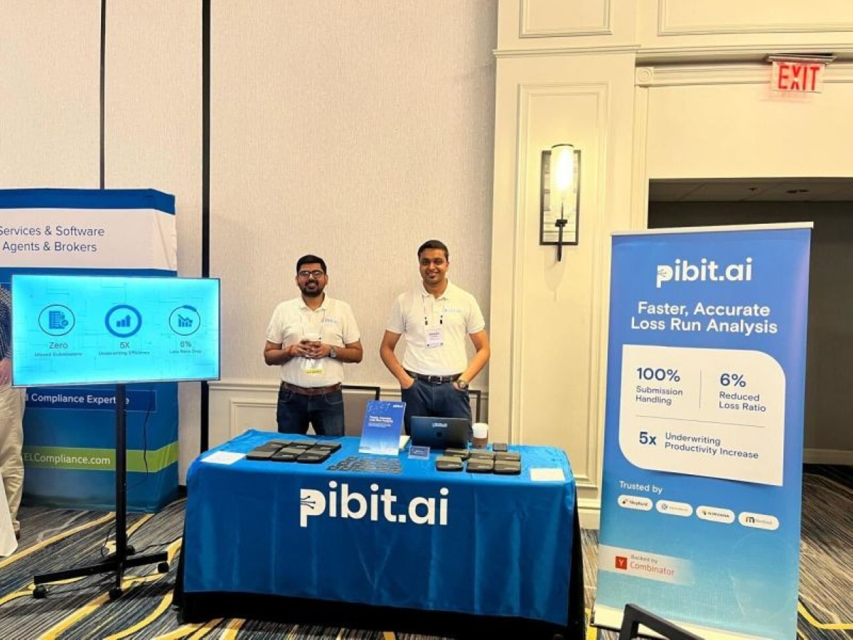 Two pibit.ai team members at a fintech conference booth, standing behind a branded table and banner promoting AI-powered loss run analysis and underwriting productivity.