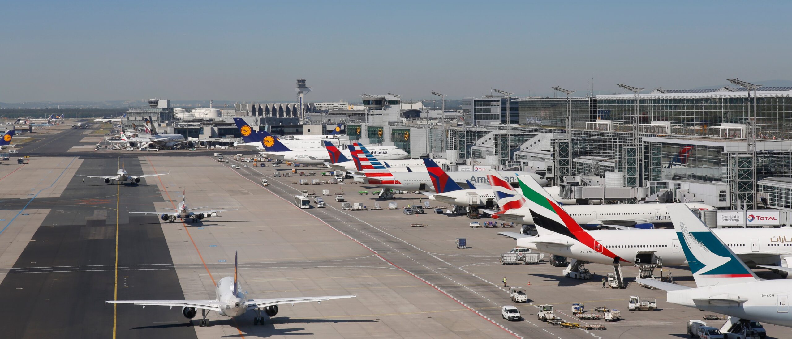 Busy international airport terminal with multiple commercial airplanes parked at gates and service vehicles on the tarmac, showing high air travel traffic.
