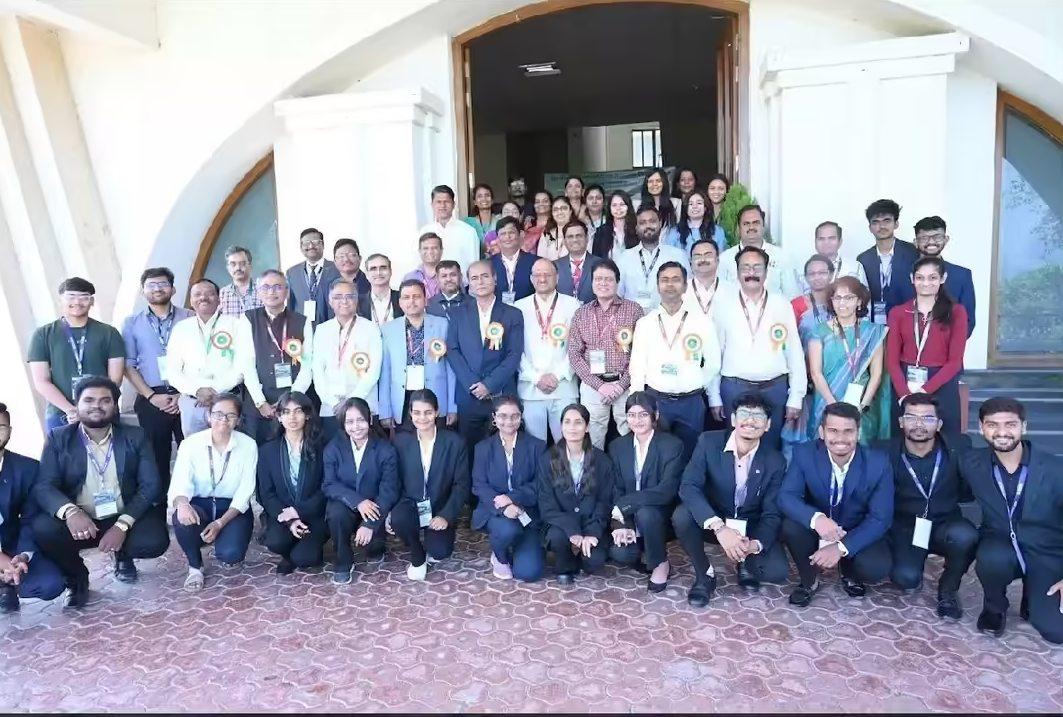 Large group photo of conference participants and graduates in formal attire gathered outside a building entrance during a business or academic event.