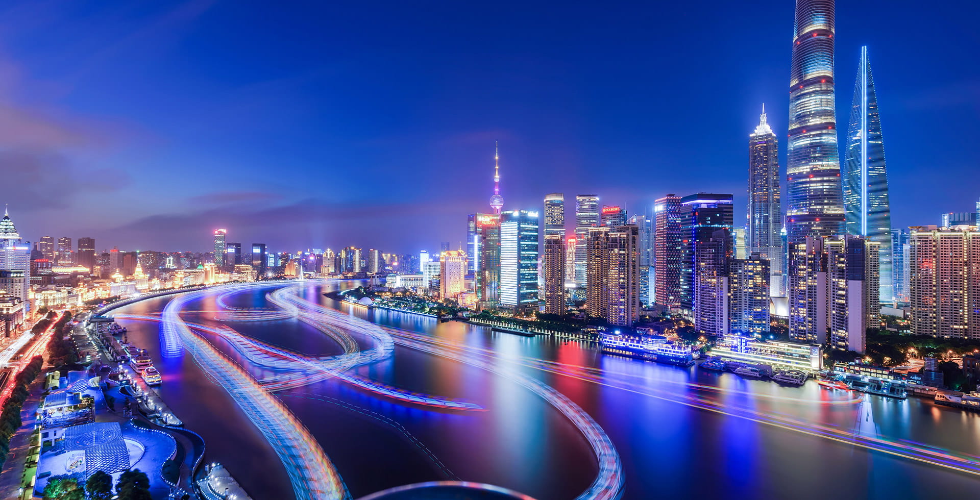 Shanghai Pudong skyline at night with Shanghai Tower and Huangpu River light trails, showcasing China’s modern financial district.