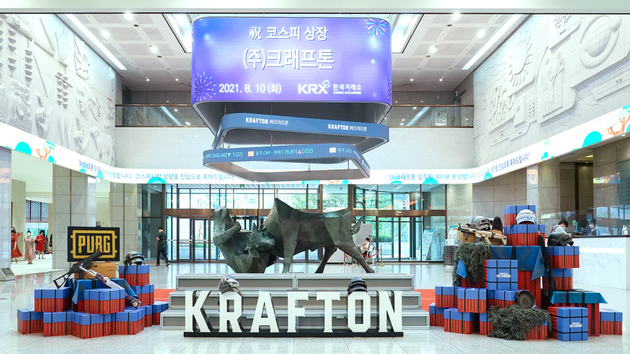 Interior of the Korea Exchange building decorated for Krafton’s KOSPI listing, featuring a central bull sculpture, large ‘KRAFTON’ lettering, PUBG-themed display props, and an overhead digital board announcing the August 10, 2021 listing.
