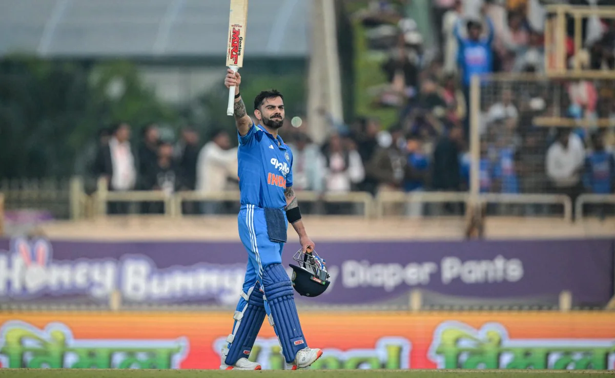 Indian cricketer in blue national team kit raises his bat to acknowledge the crowd after a milestone innings in a stadium.