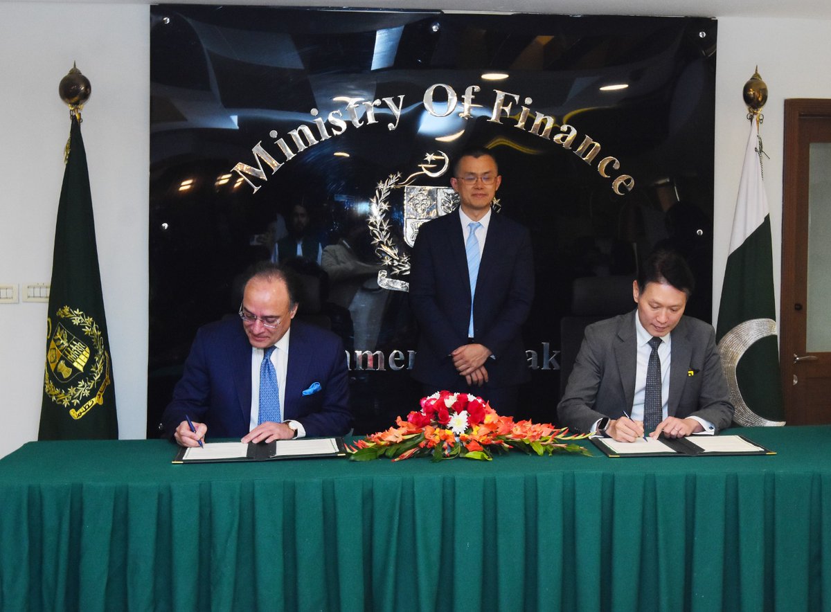 Officials from Pakistan’s Ministry of Finance signing a formal agreement at a ceremony, with national flags, a floral arrangement, and the Ministry of Finance emblem displayed behind them.