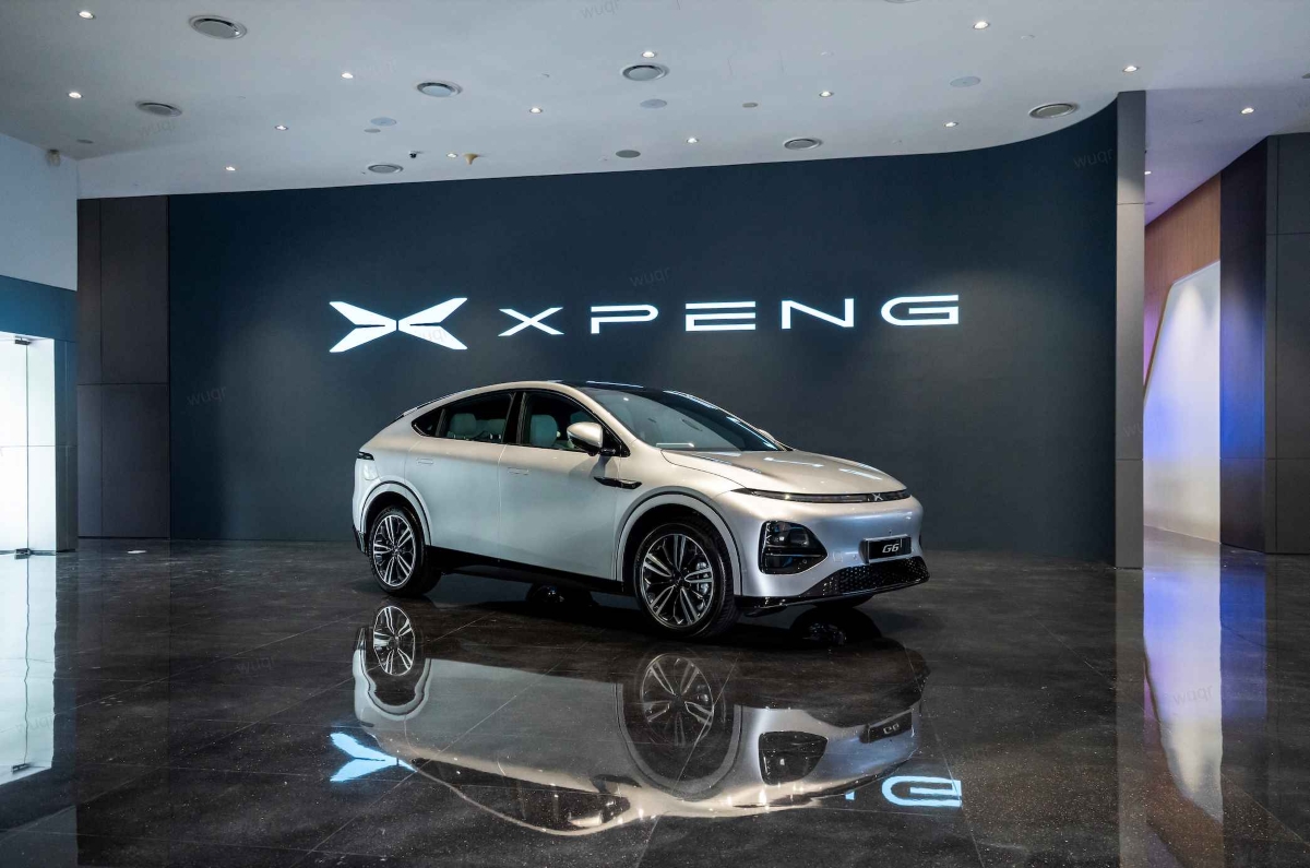 XPeng G6 electric SUV displayed in a modern showroom, featuring the XPeng logo on the wall and a silver vehicle showcased on a reflective floor.