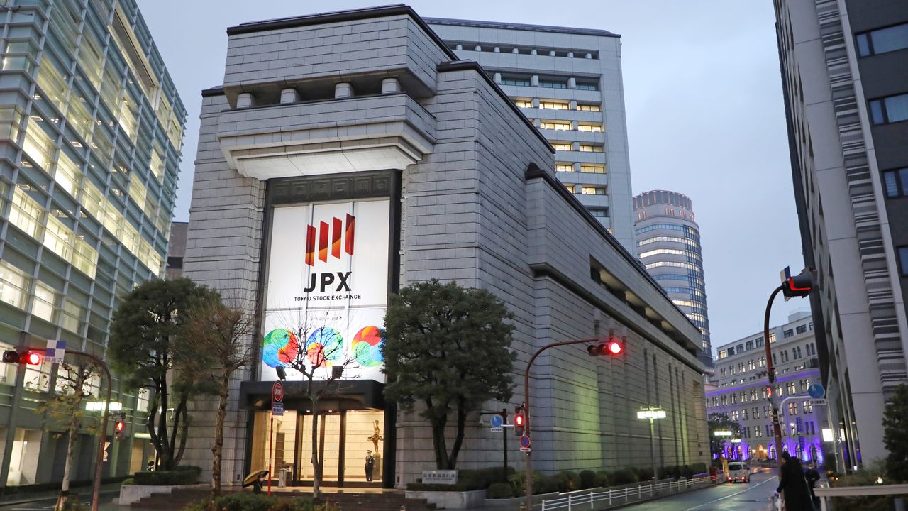 Exterior view of the Tokyo Stock Exchange (JPX) building in central Tokyo, Japan, showing its stone façade, illuminated JPX logo, and surrounding office towers at dusk.
