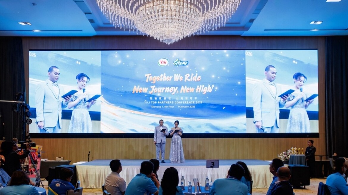 Corporate conference event with hosts on stage under a large LED screen reading “Together We Ride, New Journey, New High,” showcasing a brand partner conference with audience seating, awards table, and formal presentation setting.
