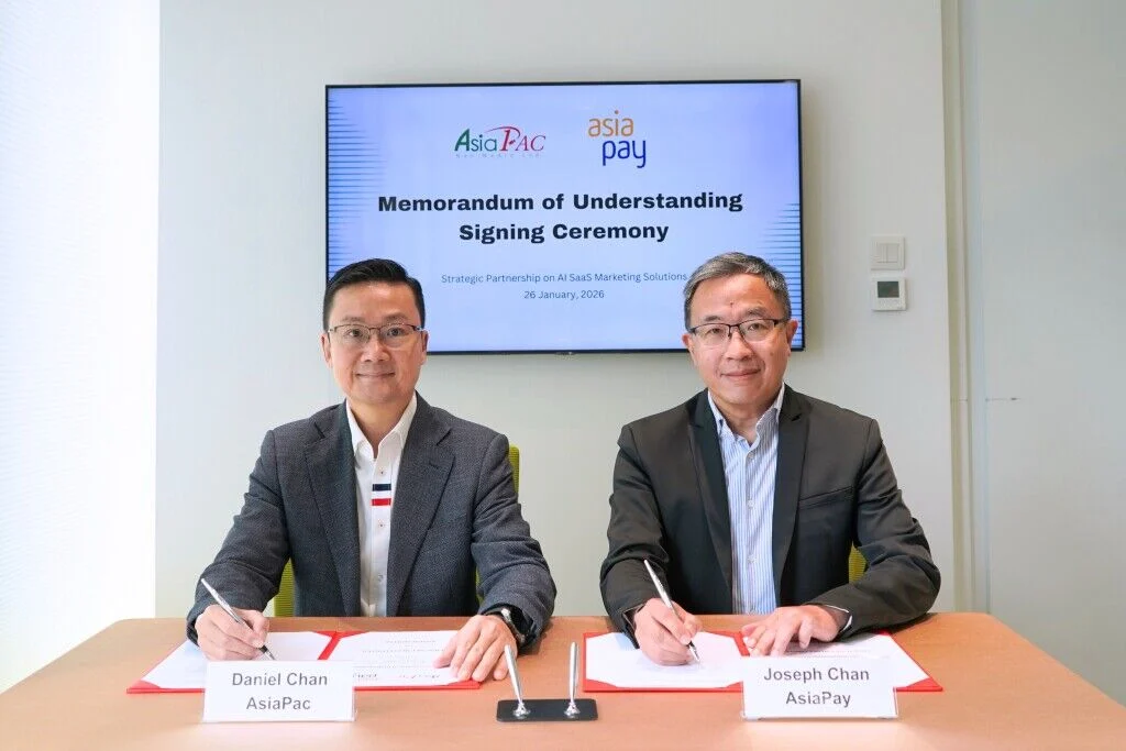 Two business executives signing a memorandum of understanding at a formal partnership ceremony between AsiaPac and AsiaPay, with a presentation screen highlighting strategic collaboration in Asia-Pacific fintech and SaaS marketing solutions.