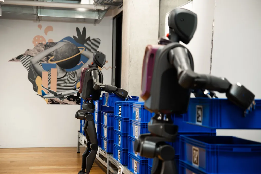 Humanoid robots sorting storage crates in an automated warehouse environment.