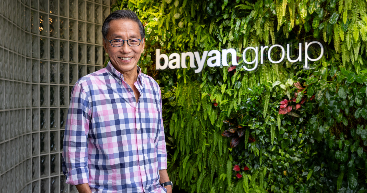 Senior executive standing in front of the Banyan Group logo and a green living wall, highlighting leadership in Asia’s hospitality sector and the company’s sustainability-focused corporate culture.