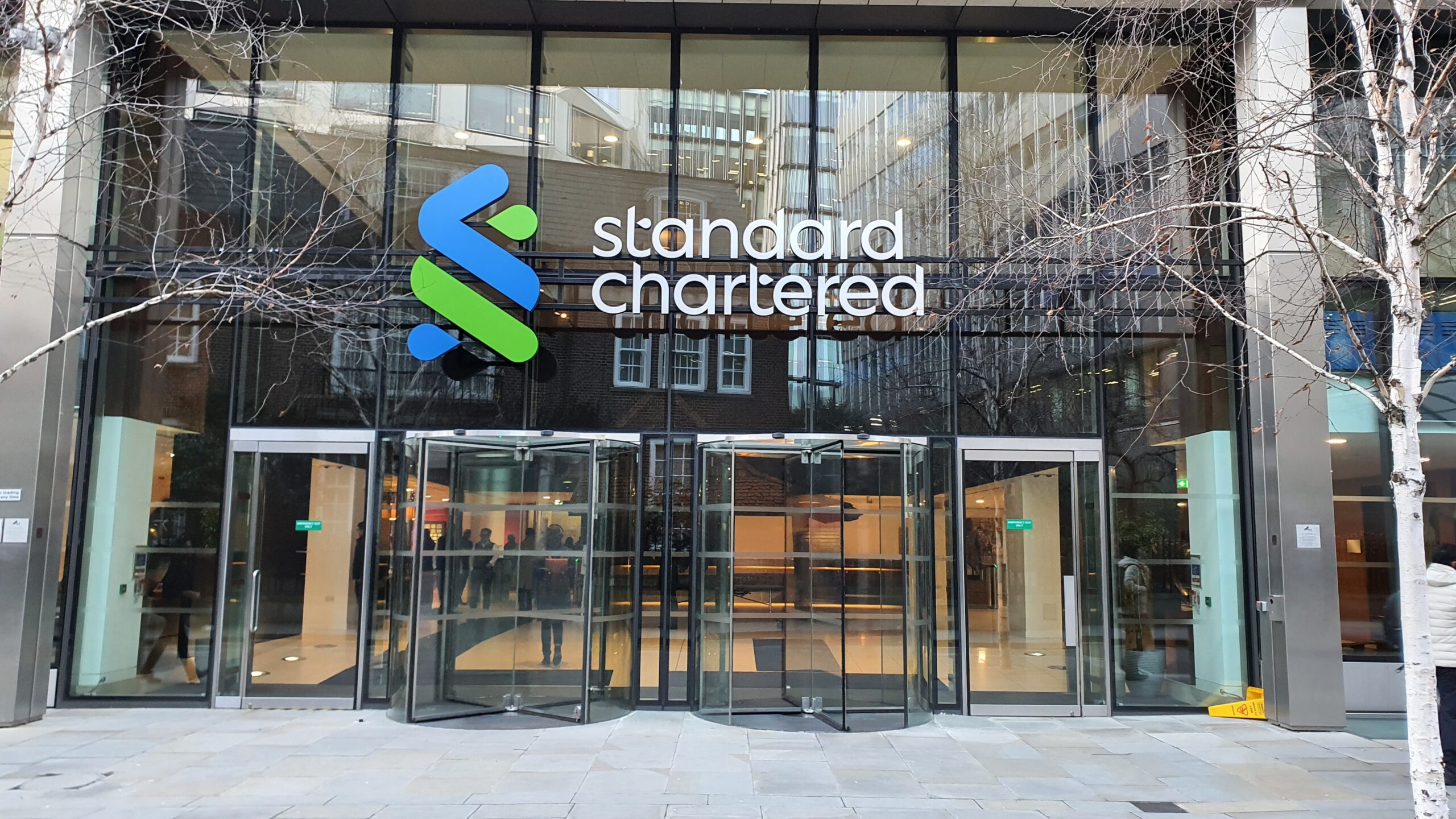 Exterior of a Standard Chartered bank office with prominent logo and glass entrance, highlighting the global banking group’s corporate presence and international financial services operations.