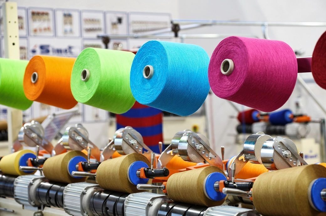 Colorful yarn spools aligned on textile manufacturing machinery, showcasing industrial thread production, fabric processing, and modern textile factory operations.