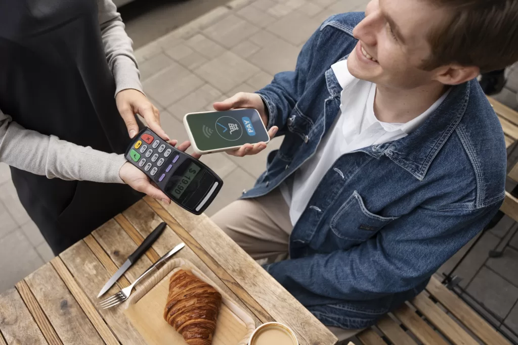 Customer making a contactless mobile payment using a smartphone at a café, illustrating digital wallet usage, cashless transactions, and modern fintech payment technology.