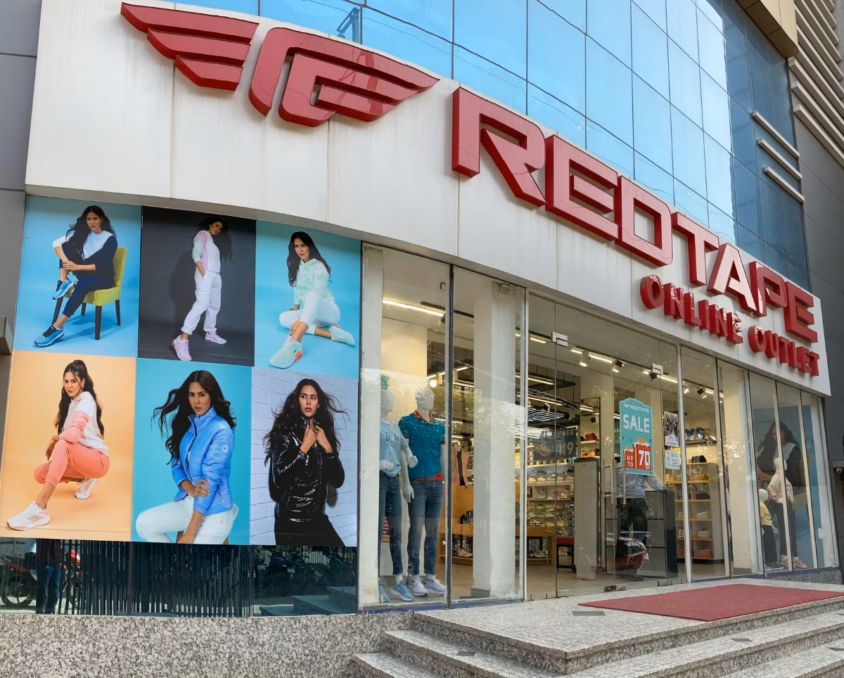 Exterior of a Red Tape retail store featuring large brand signage and window displays showcasing casual footwear and apparel, highlighting the Indian fashion brand’s offline retail presence.