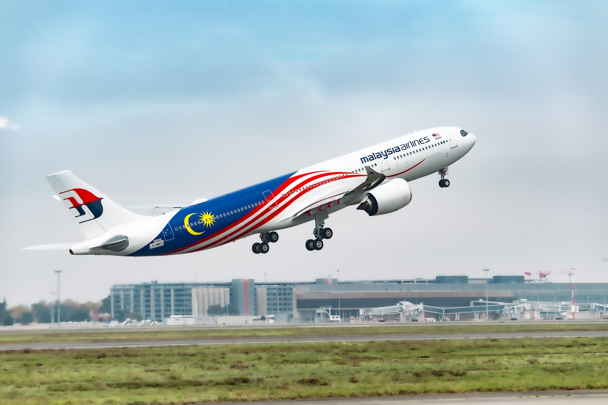 Malaysia Airlines aircraft taking off from international airport runway with Kuala Lumpur flag livery on fuselage.