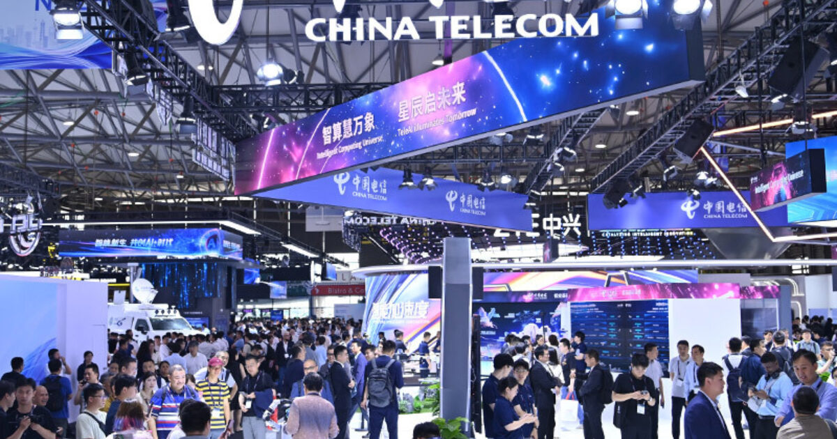 Crowded technology exhibition hall featuring China Telecom’s booth, with large digital banners, LED displays, and industry professionals networking at a major Asian telecom and innovation trade show.