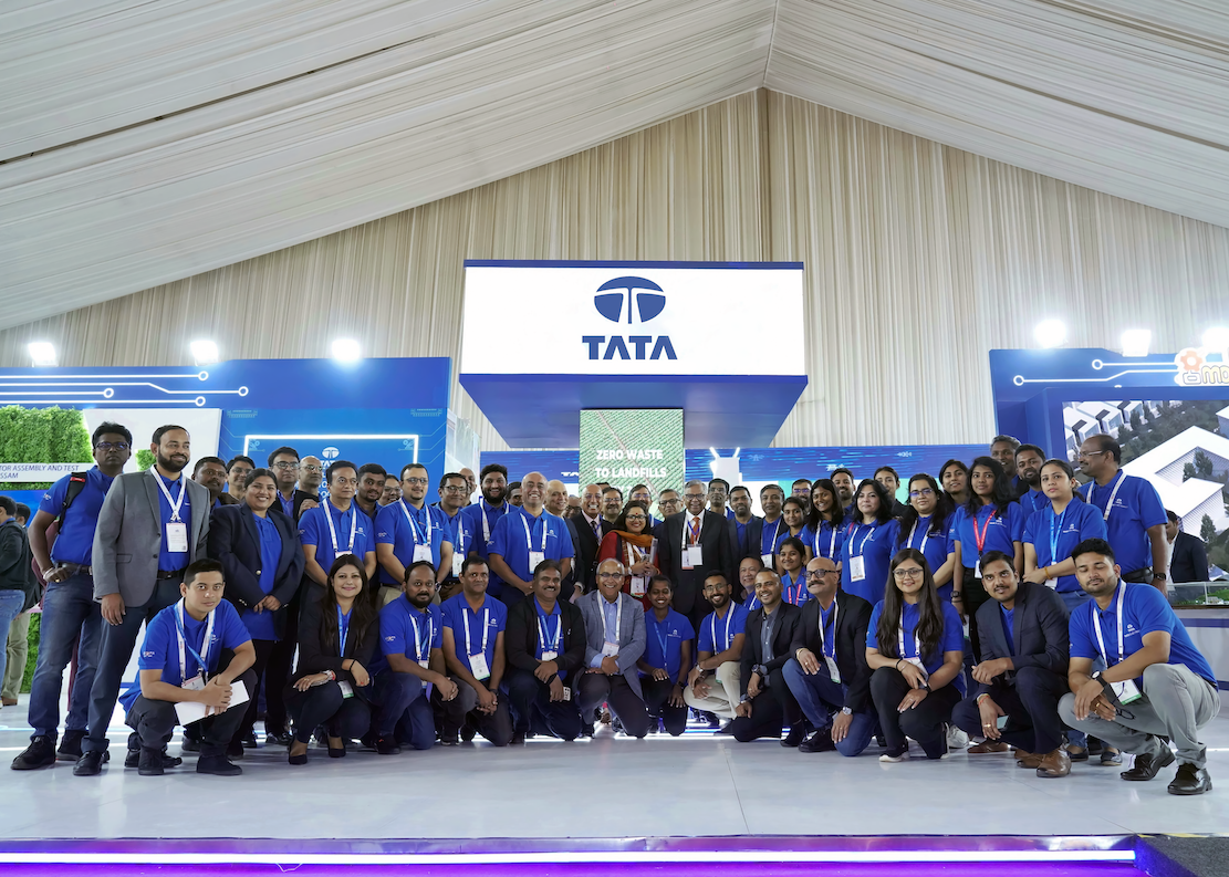Group photo of Tata Group employees and executives at a corporate technology exhibition booth, highlighting teamwork, innovation, and sustainability initiatives such as zero-waste manufacturing and digital transformation in India’s industrial sector.
