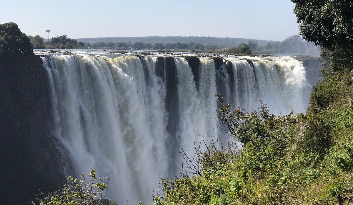 Panoramic view of Victoria Falls with powerful water cascading into the gorge, surrounded by lush greenery, showcasing one of Africa’s most iconic natural landmarks and major tourist attractions.