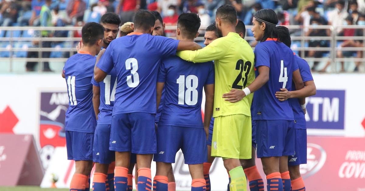 Football team in blue jerseys huddling together on the pitch before kickoff, showing teamwork and match preparation during a competitive game.