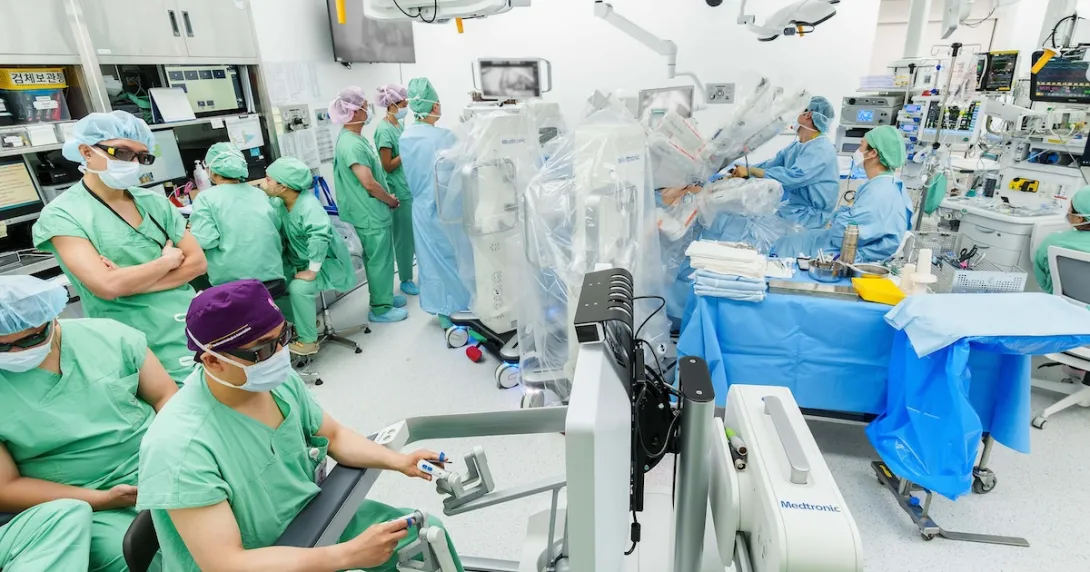 Medical team performing a robotic-assisted surgery in a modern hospital operating room with surgeons monitoring the procedure through advanced surgical consoles and equipment.