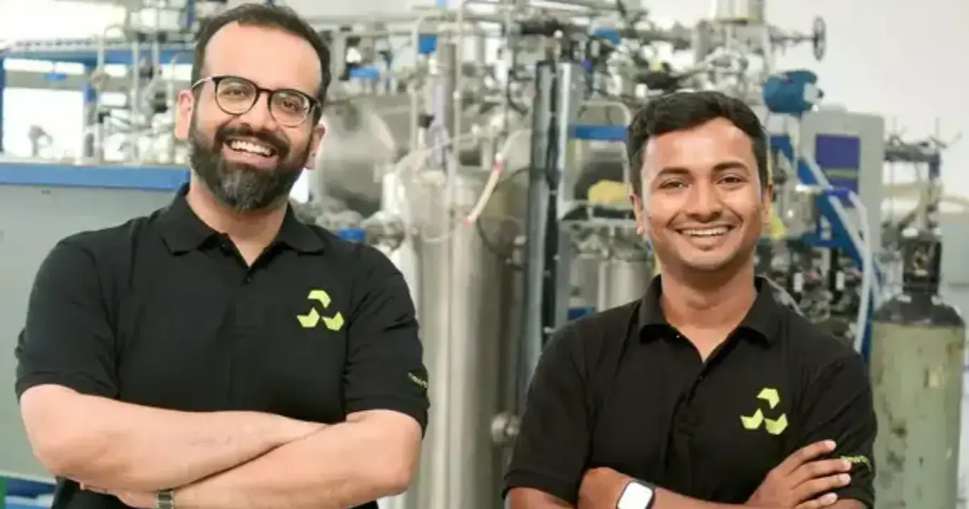 Two startup founders standing in a laboratory facility with advanced industrial equipment, representing innovation in biotechnology and clean technology manufacturing.
