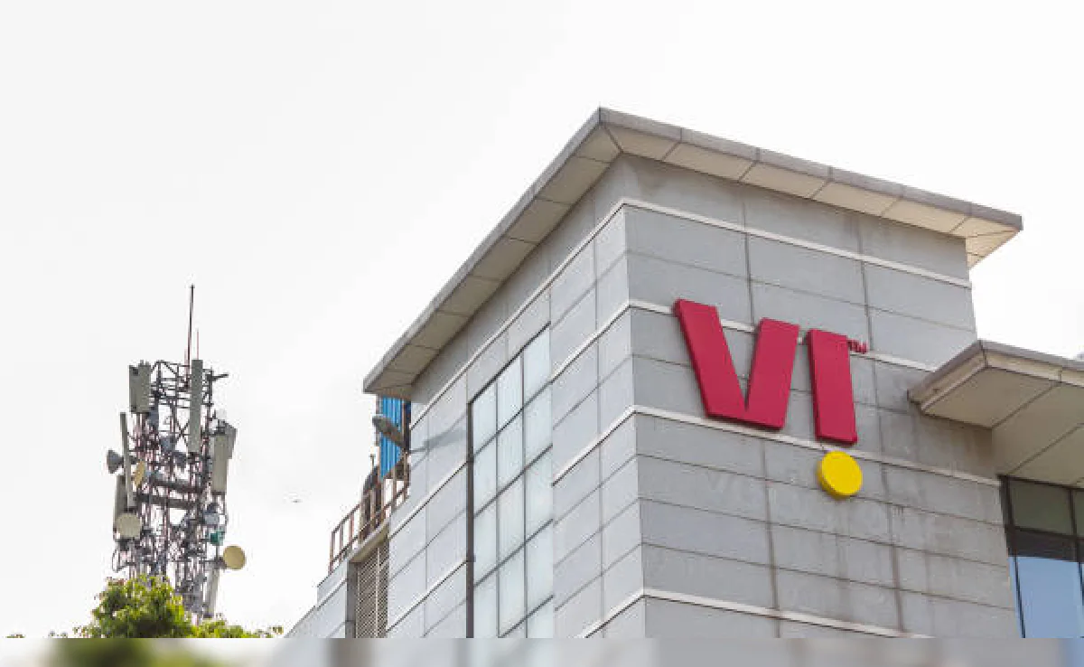 Vodafone Idea (Vi) logo displayed on a telecommunications company building with a nearby mobile network tower infrastructure.