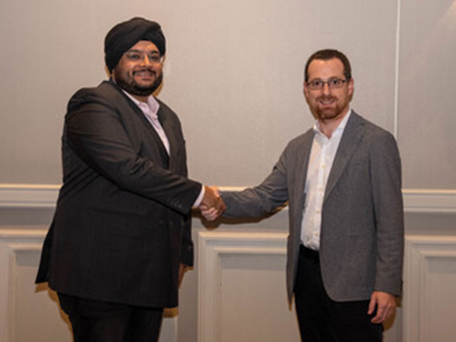 Two business executives shake hands during formal meeting, marking strategic partnership agreement in corporate setting.