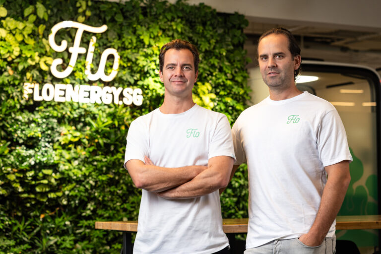 FLO Energy founders Matthijs Guichelaar and Ernst Westendorp standing in front of a green wall with the FLO Energy logo in their Singapore office.