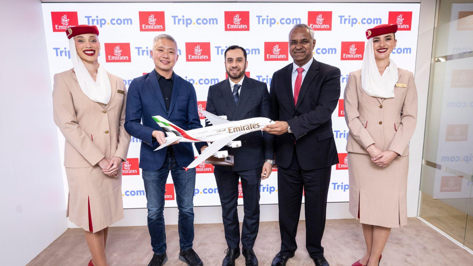 Trip.com and Emirates executives pose with a model airplane during a partnership event, flanked by Emirates cabin crew in uniform.
