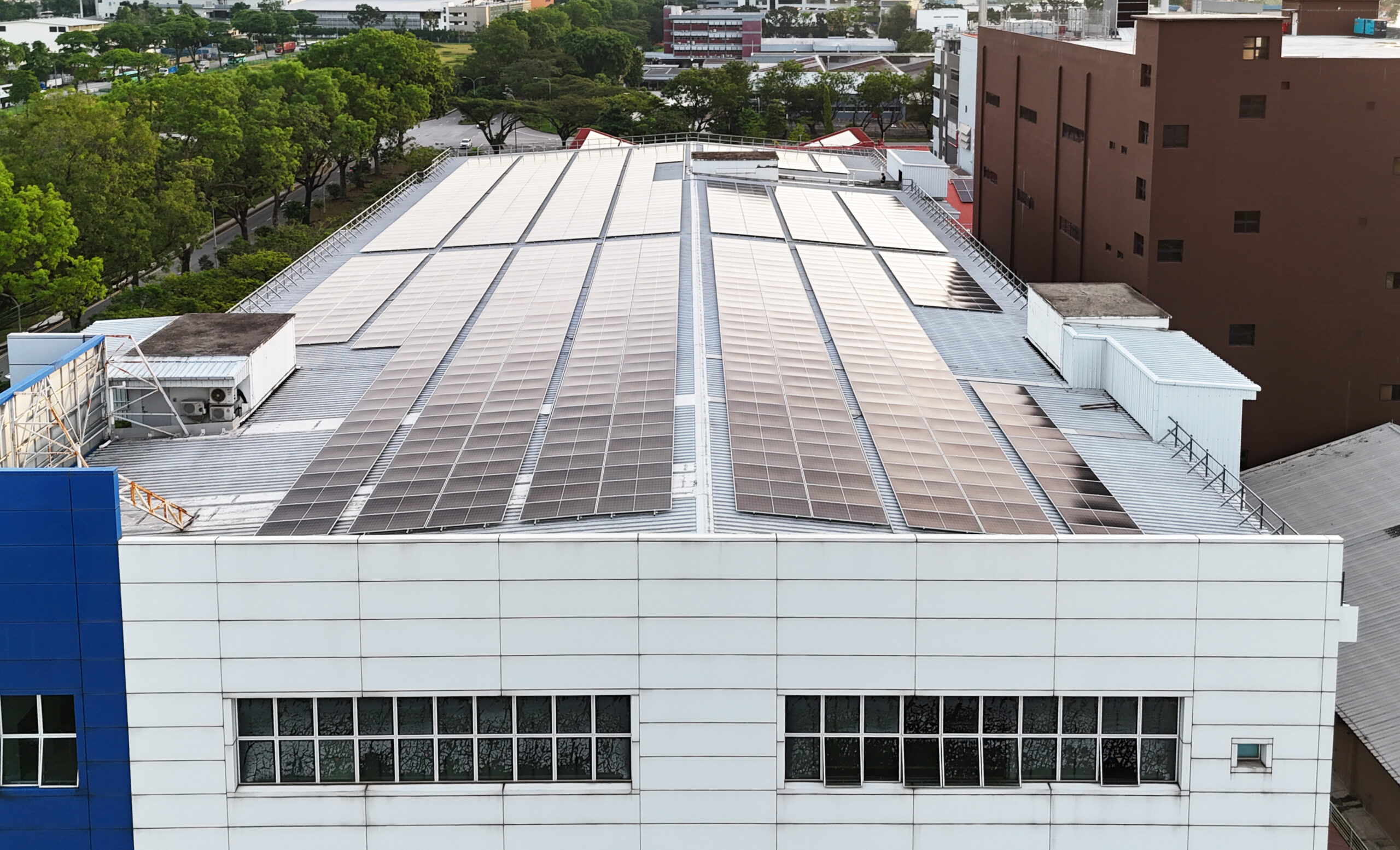 Aerial view of an extensive solar panel array on the rooftop of a modern industrial building in Singapore.