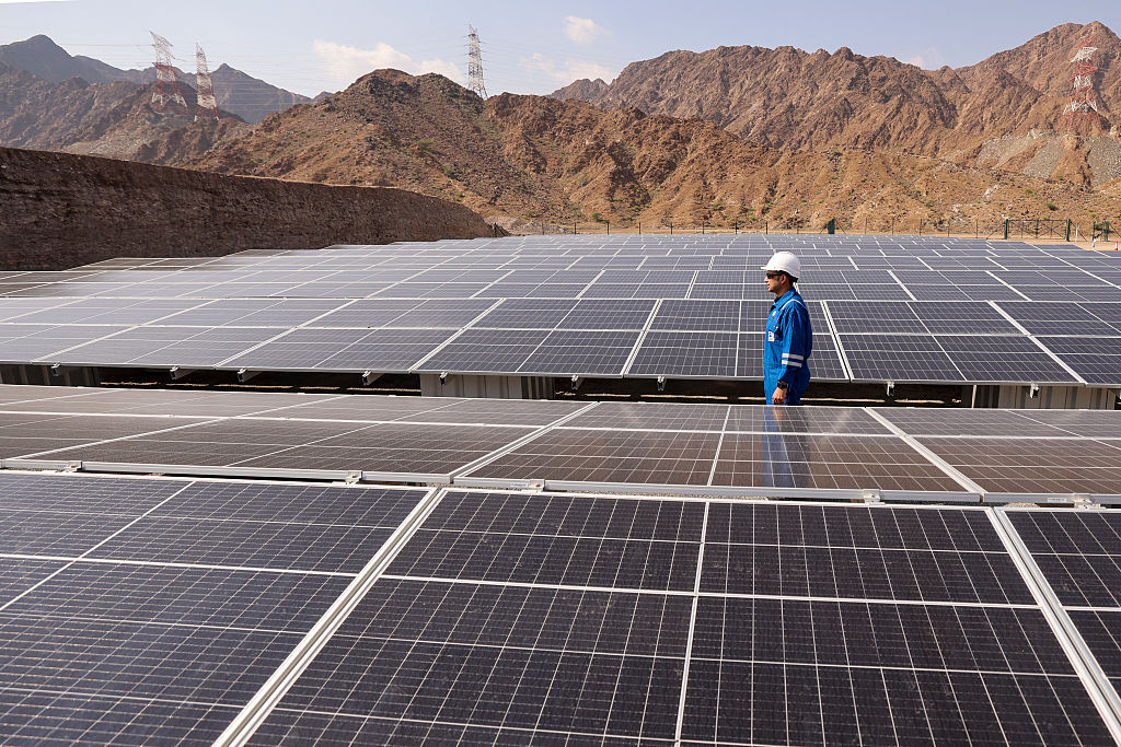 Technician inspecting large solar panel installation in a desert landscape with mountains, highlighting renewable energy infrastructure.