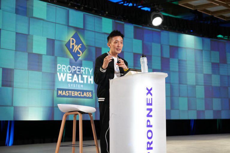 Kelvin Fong speaking at a Property Wealth System masterclass, standing at a PropNex podium with a presentation screen behind him.