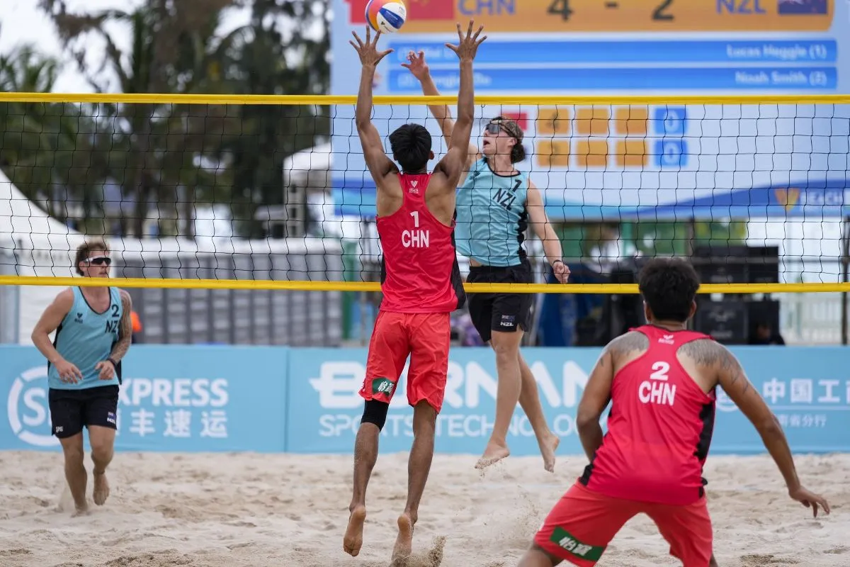 Beach volleyball match with Chinese team players competing at the net, highlighting international sports competition, teamwork, and athletic performance on sand court.