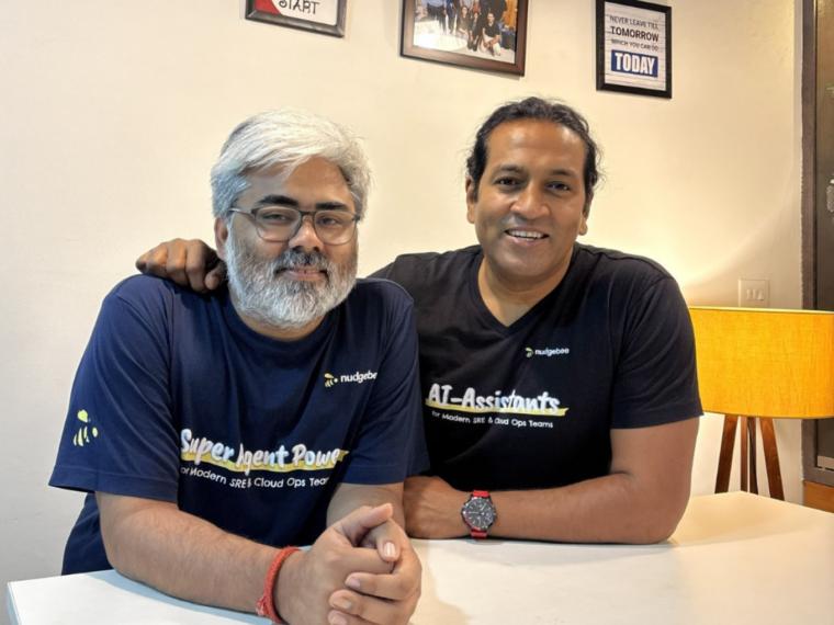Two tech professionals posing together indoors, wearing AI and cloud computing themed t-shirts, representing startup founders and enterprise technology collaboration.
