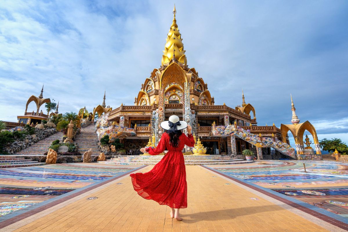Tourist in red dress walking toward Wat Phra That Pha Sorn Kaew temple in Thailand, showcasing cultural tourism, ornate architecture, and scenic travel destination.