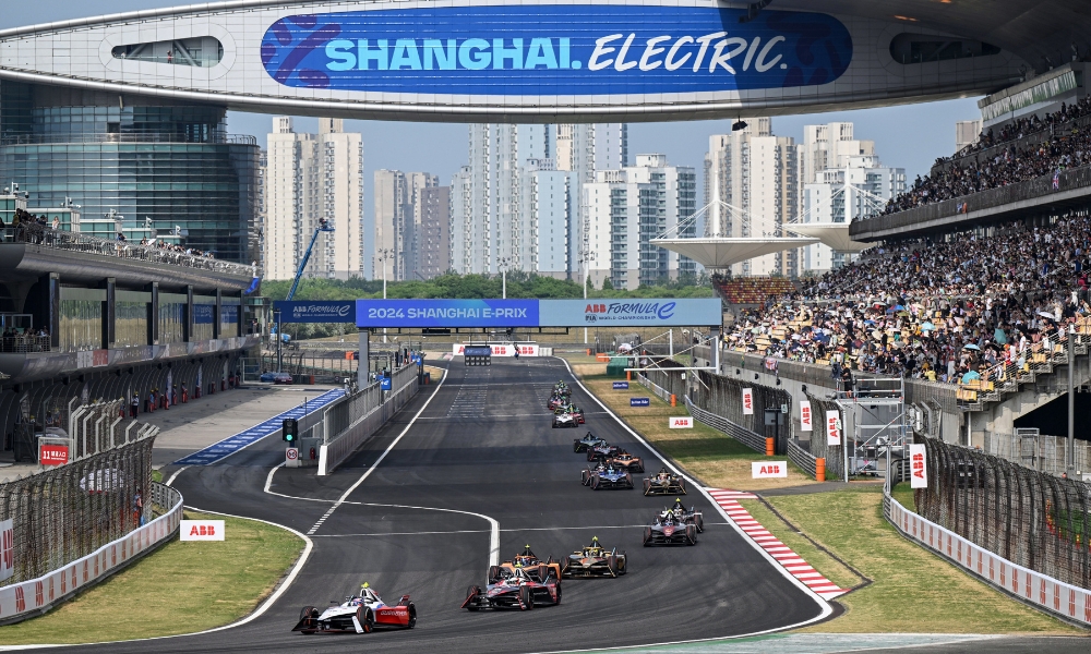 Formula E race at Shanghai E-Prix 2024, electric cars competing on urban circuit with Shanghai skyline and grandstand crowd in view.