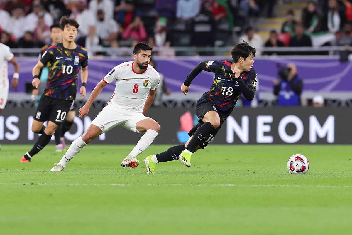 International football match action with South Korea player sprinting past defender, highlighting competitive soccer gameplay, athletic performance, and tournament atmosphere.