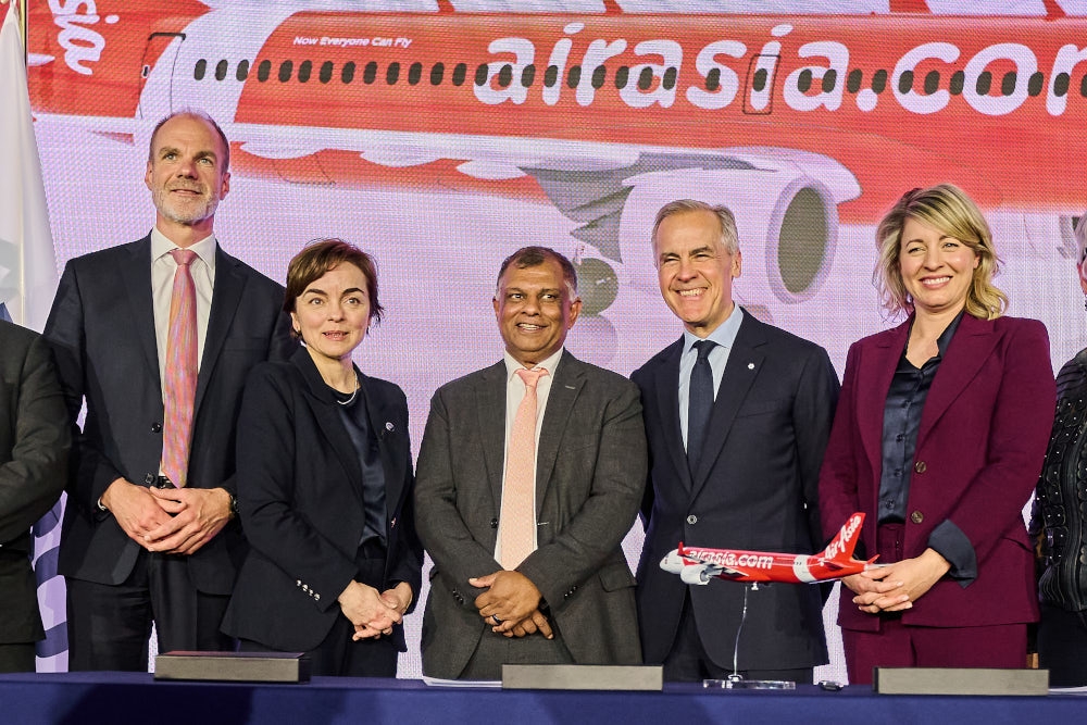 AirAsia executives and international partners posing during a corporate aviation event, standing in front of an AirAsia aircraft display and model plane highlighting airline expansion and global partnerships.