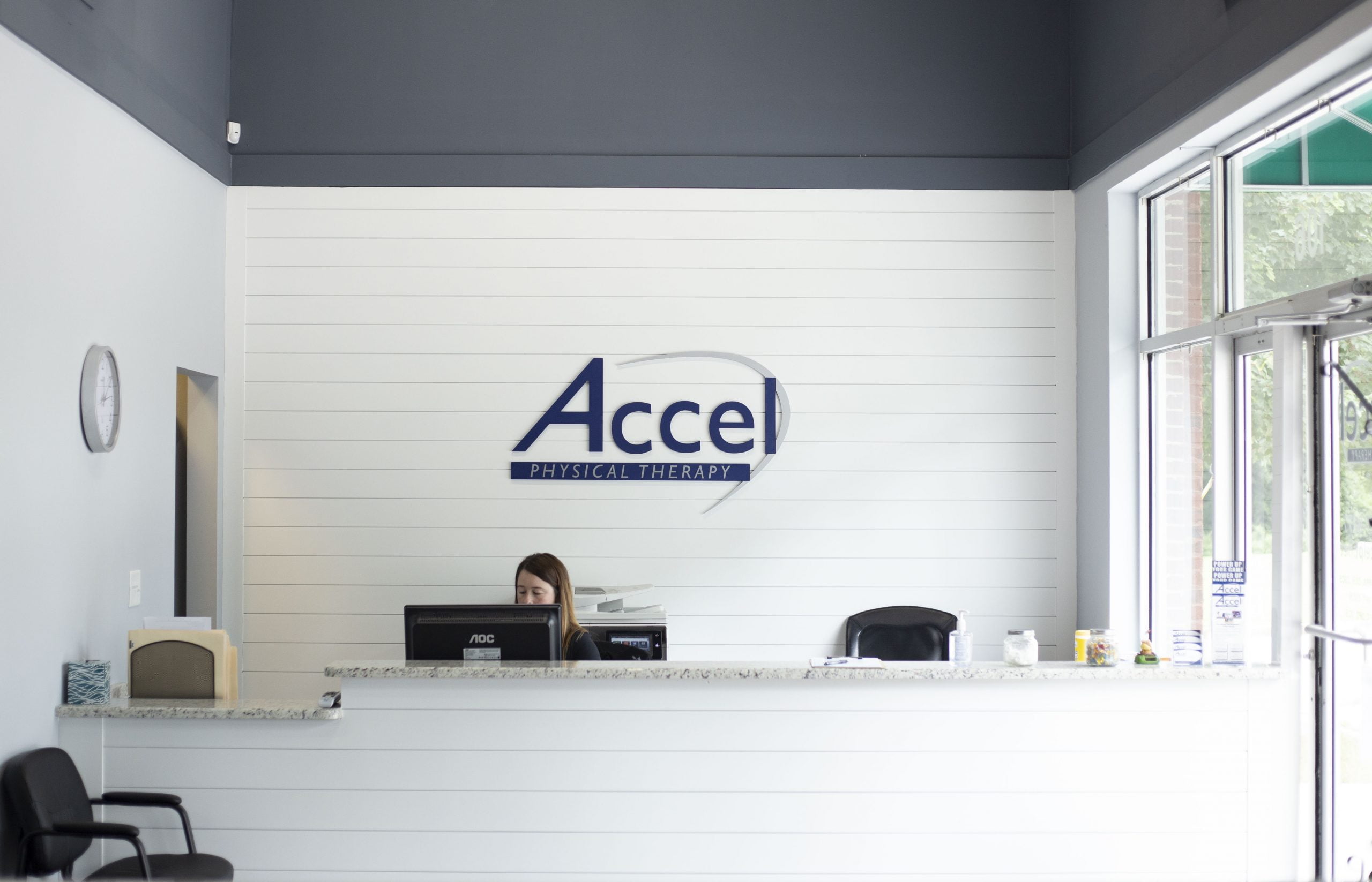 Reception area of Accel Physical Therapy clinic with front desk staff, clean modern interior, and healthcare branding focused on rehabilitation services.
