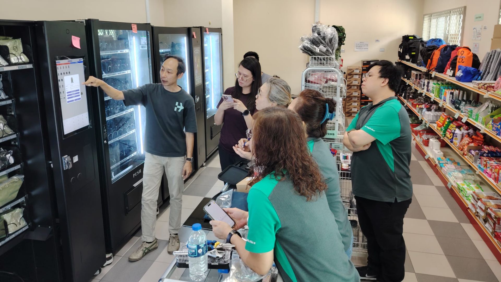 Staff demonstrating how to use a smart vending machine to a group of people inside a retail environment.